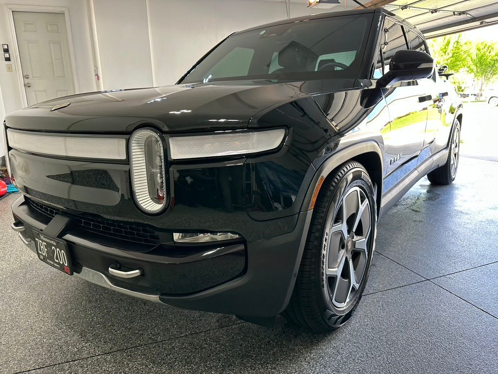 Black Rivian SUV parked in a garage, front view, sleek design with light bar across the front.