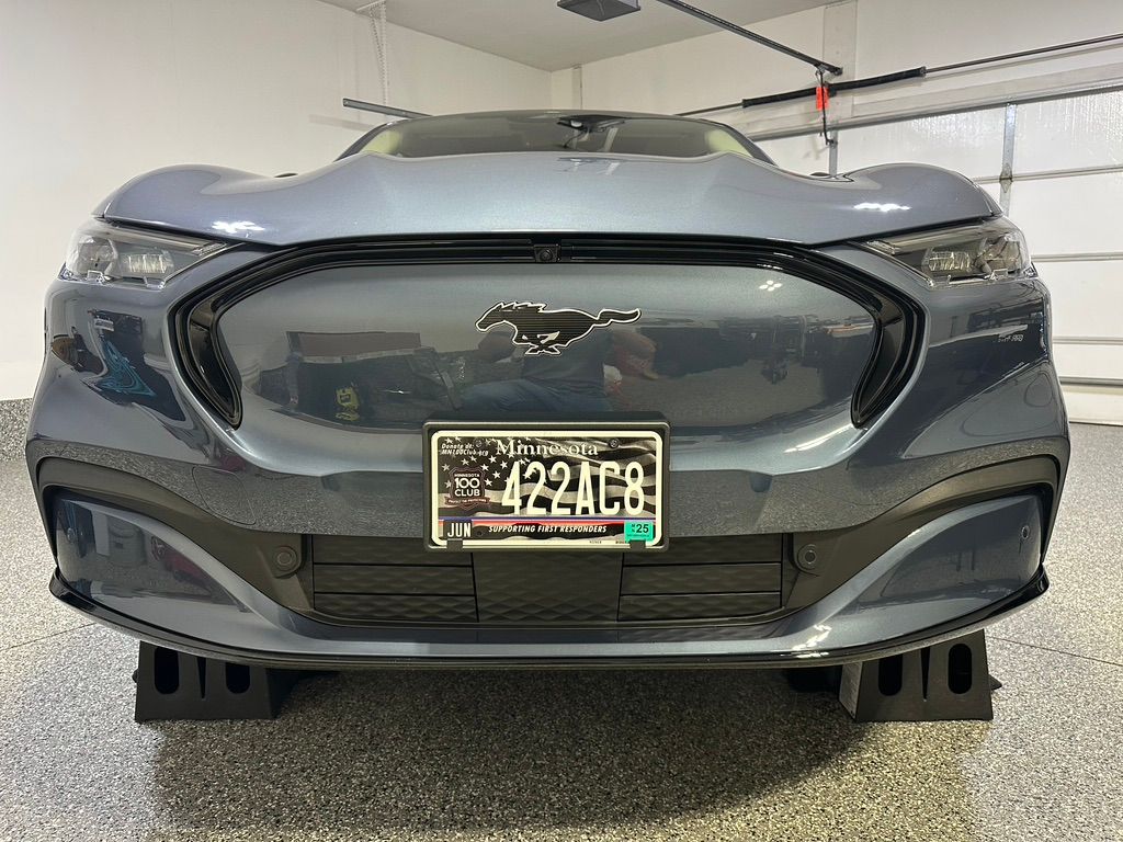 A blue Ford Mustang Mach-E parked on black blocks in a garage, front view with a license plate.
