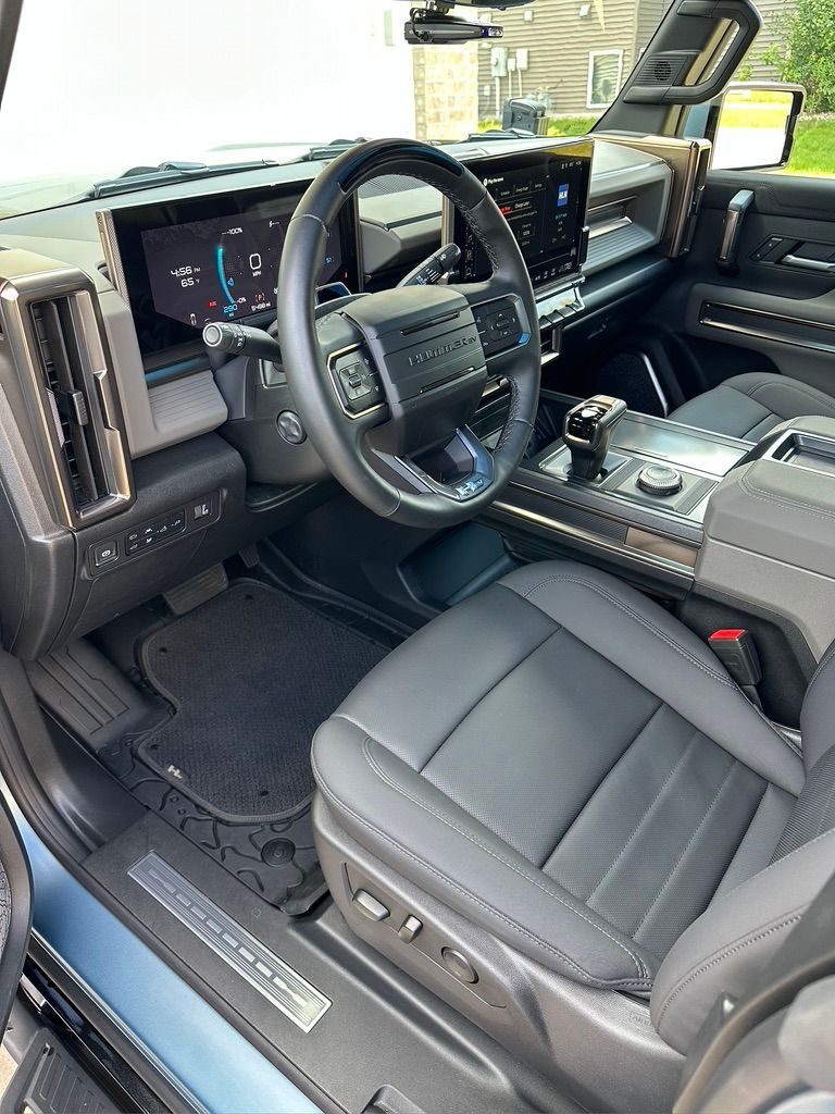 Interior view of a blue GMC Hummer EV. Black leather seats, digital displays, and a black steering wheel are visible.