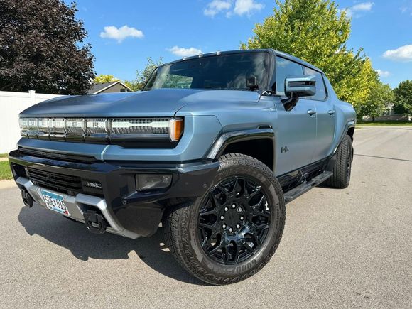 Blue GMC Hummer EV truck parked on a paved street, sunny day.