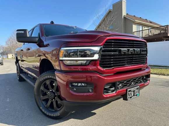 Red RAM truck parked in front of a house on a sunny day. Black wheels and grille.