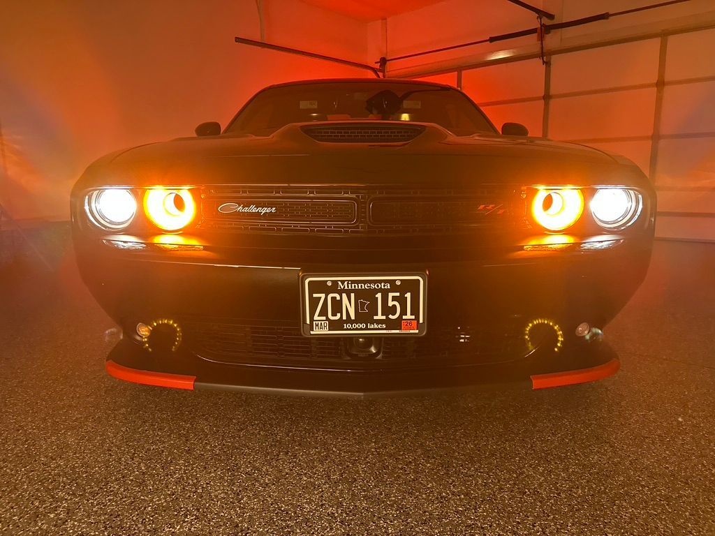 Black Dodge Challenger with bright orange/white headlights in a garage.