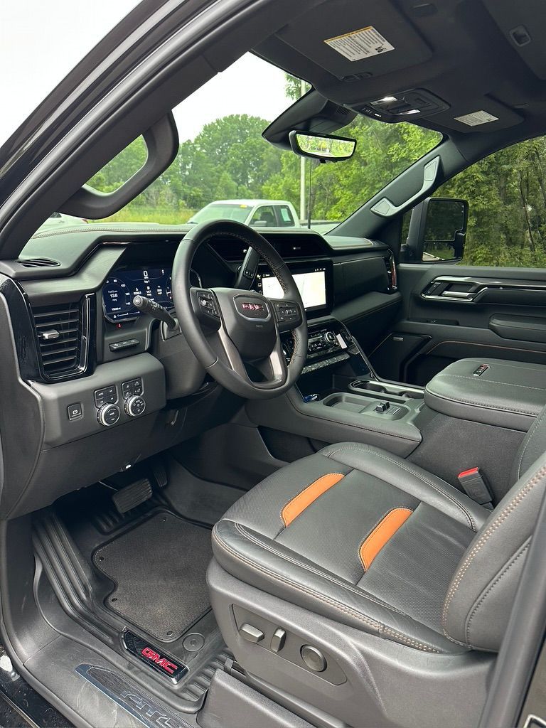 Interior of a black GMC truck; black and orange leather seats, dashboard with digital display, steering wheel.