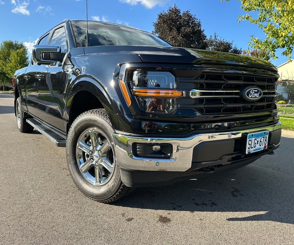 Black Ford F-150 pickup truck parked on a paved street. Chrome accents, front view, sunny day. Minnesota license plate.