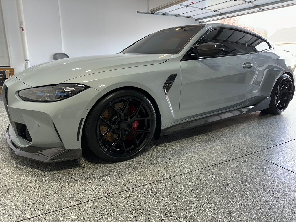 Grey BMW M4 coupe in a garage with black wheels and modifications.