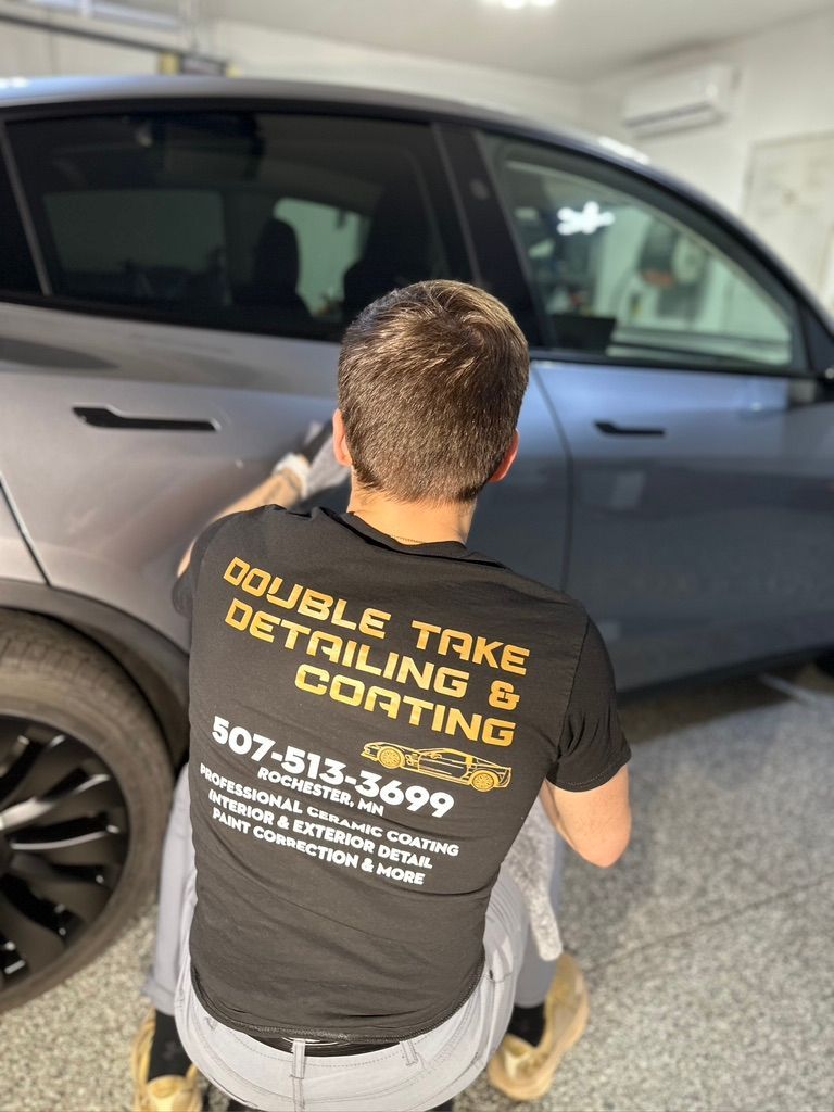 Man detailing a gray car, wearing a shirt for Double Take Detailing. Indoor setting.