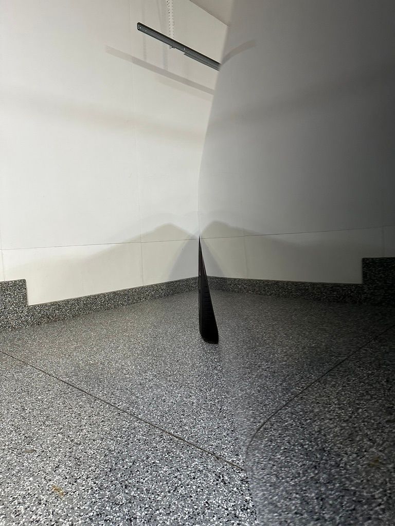 White walls meet a speckled gray floor in a garage; a dark shadow extends down the center.