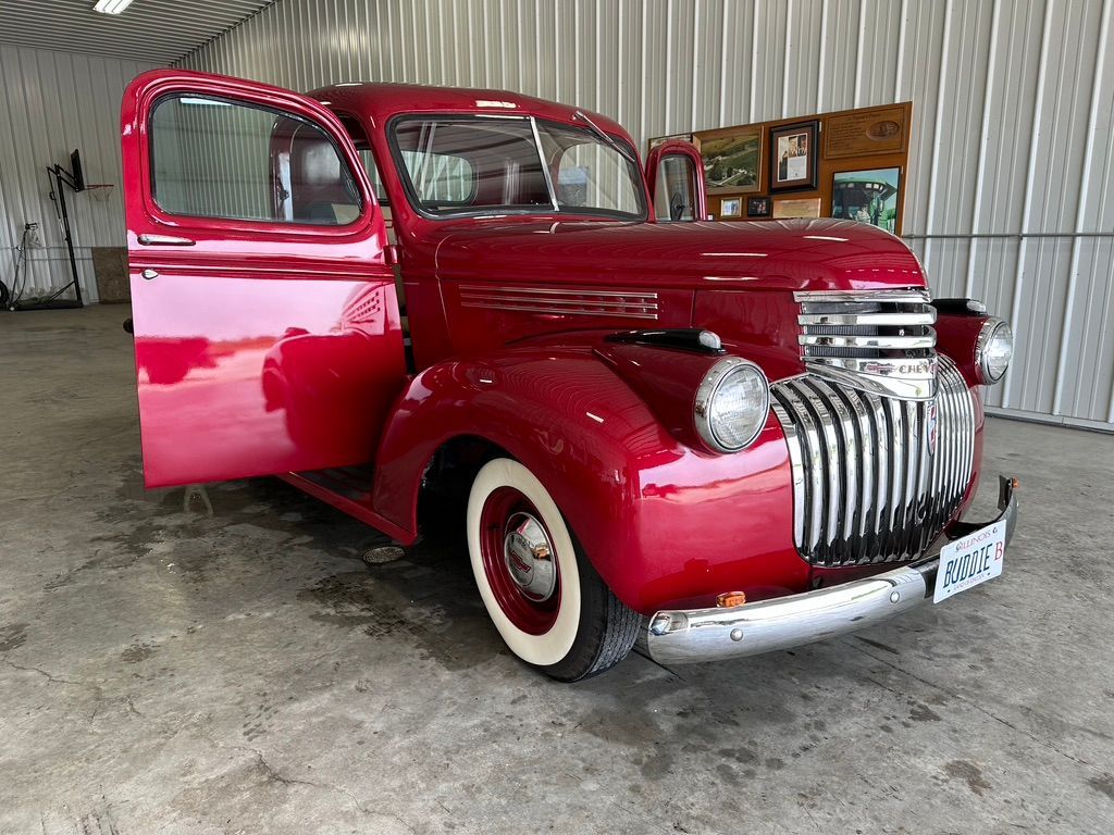 Red vintage Chevrolet truck with doors open, white tires, in a garage.