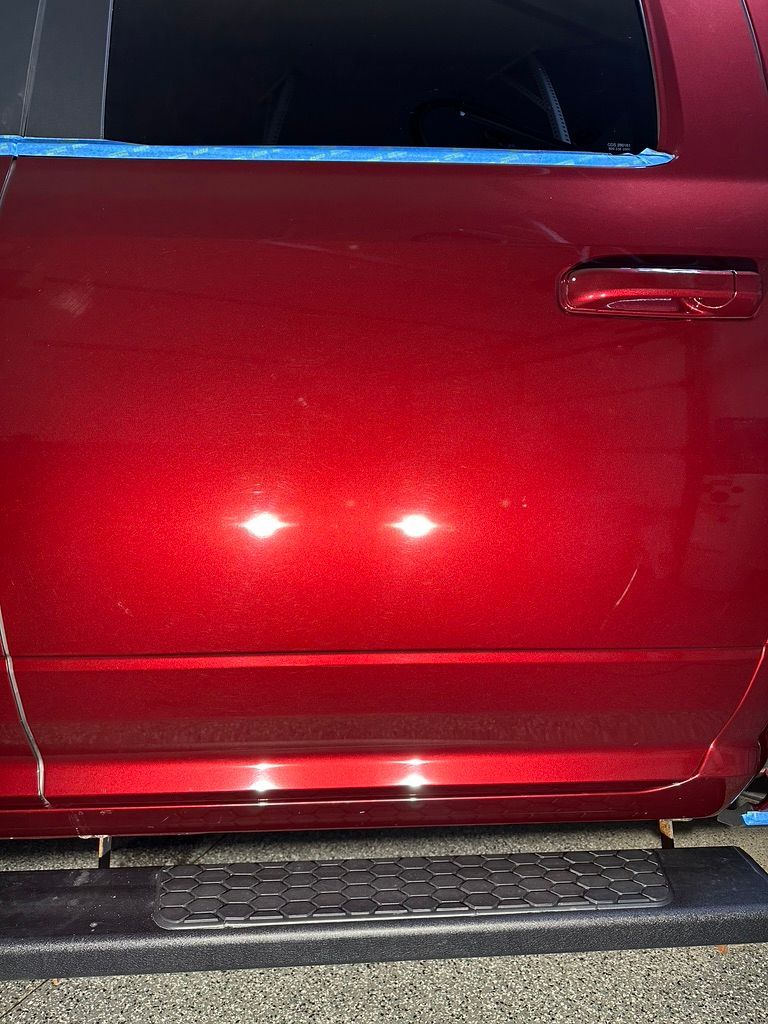 Red car door with scratches, polished and taped, showing reflections.