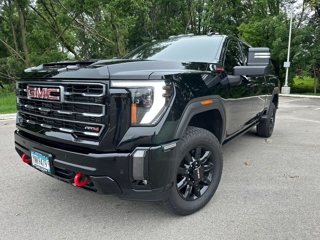 Black GMC Sierra heavy-duty truck parked outdoors. The front features a black grille and red tow hooks.