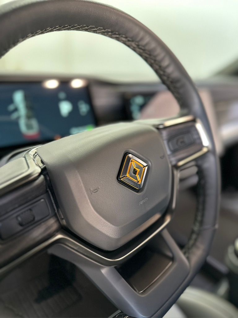 Black steering wheel with Rivian logo in a vehicle's interior.