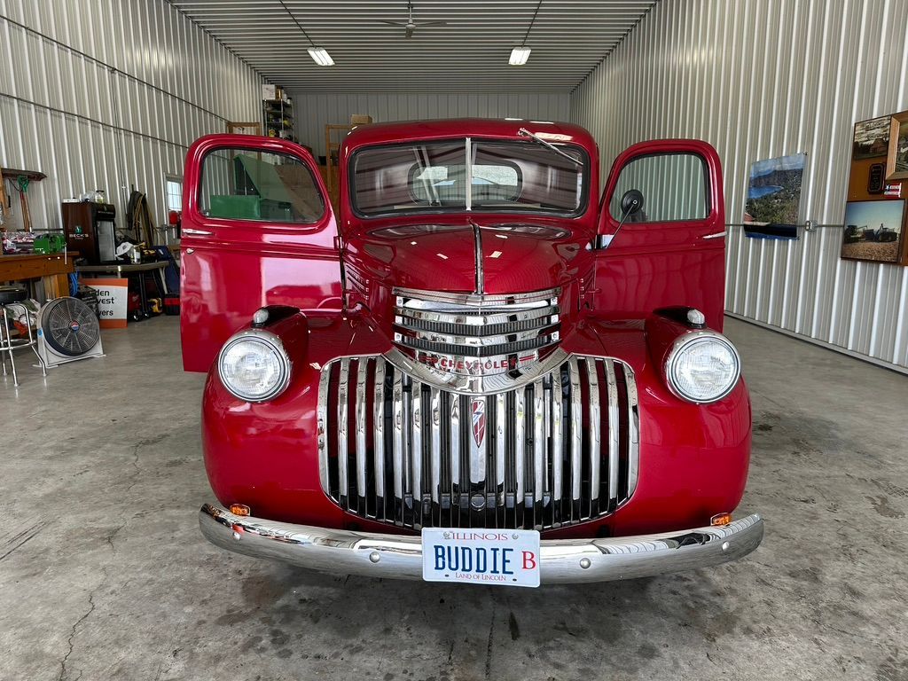 Red vintage Chevrolet truck with open doors in a garage.