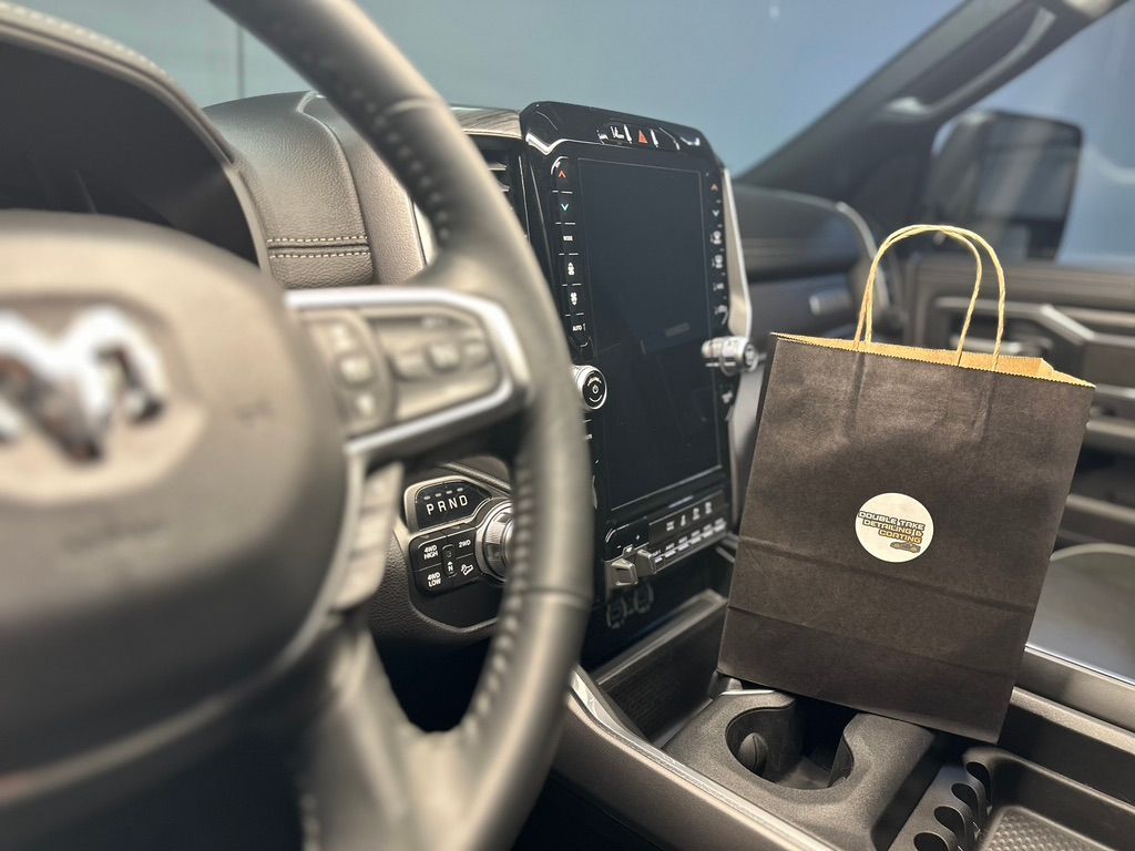A brown paper bag sits in a car's cup holder near the dashboard and steering wheel.