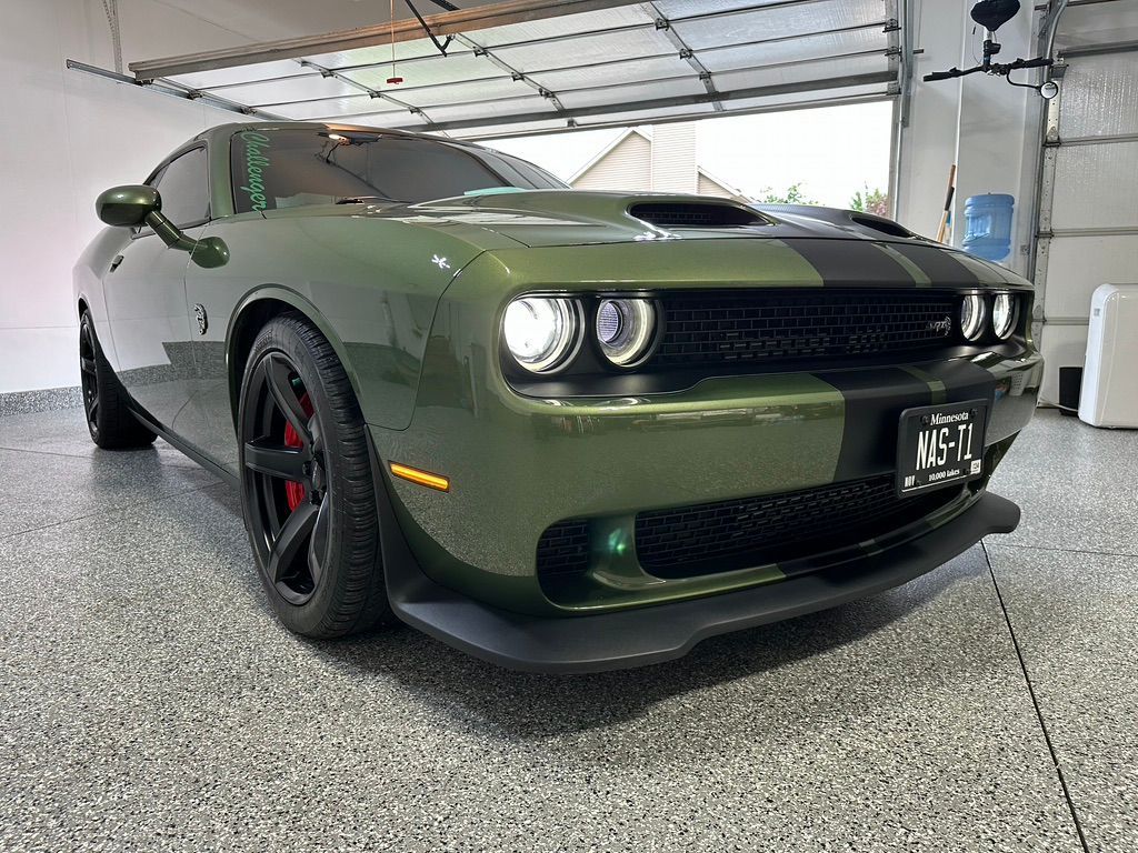 Green Dodge Challenger with black stripes, parked in a garage.