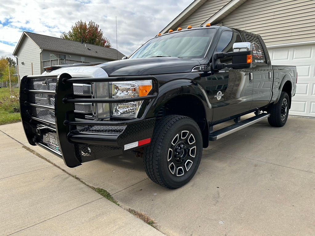 Black Ford pickup truck with a brush guard parked in a driveway near a house and garage.
