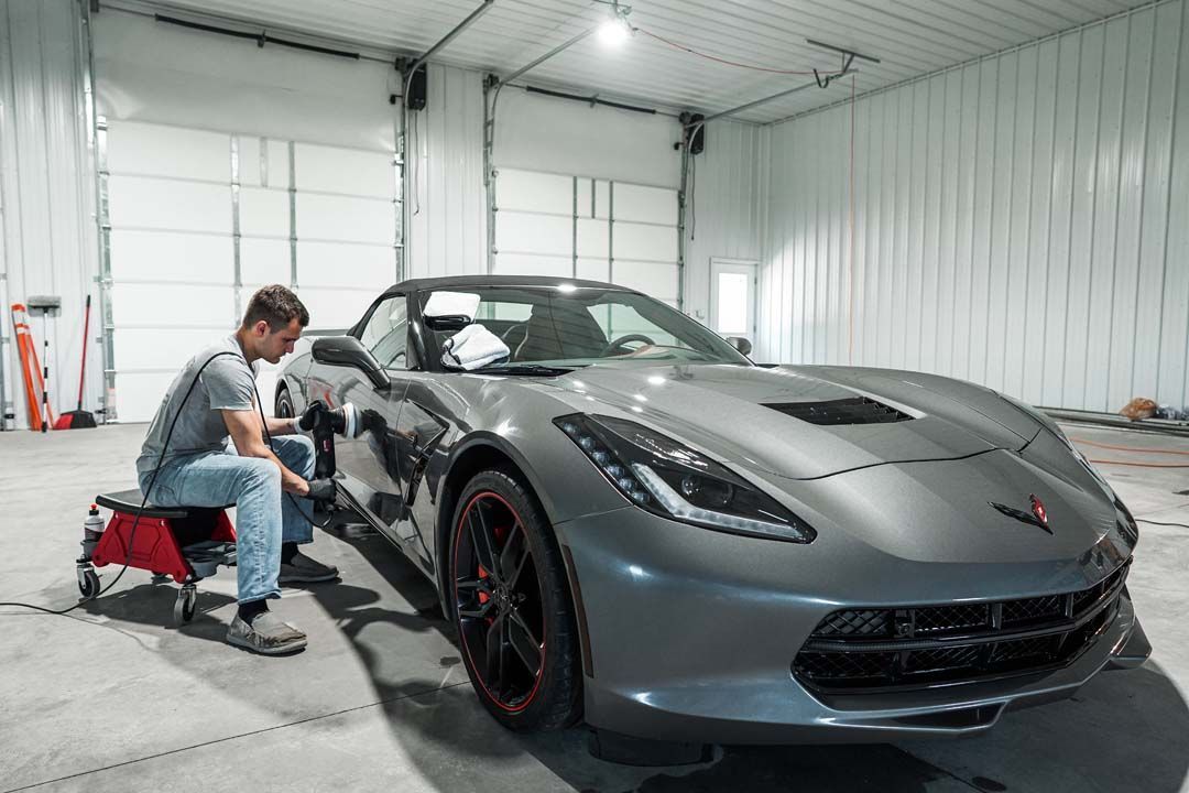 Man detailing a gray Corvette in a well-lit garage.