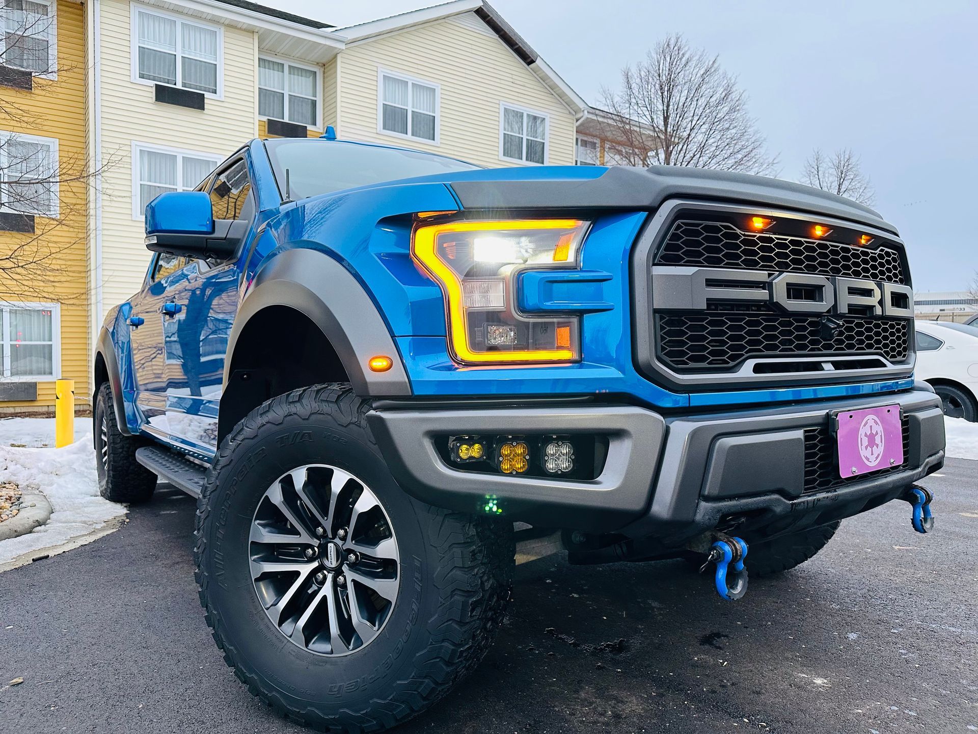 Blue Ford Raptor truck with custom lights, parked near a building.