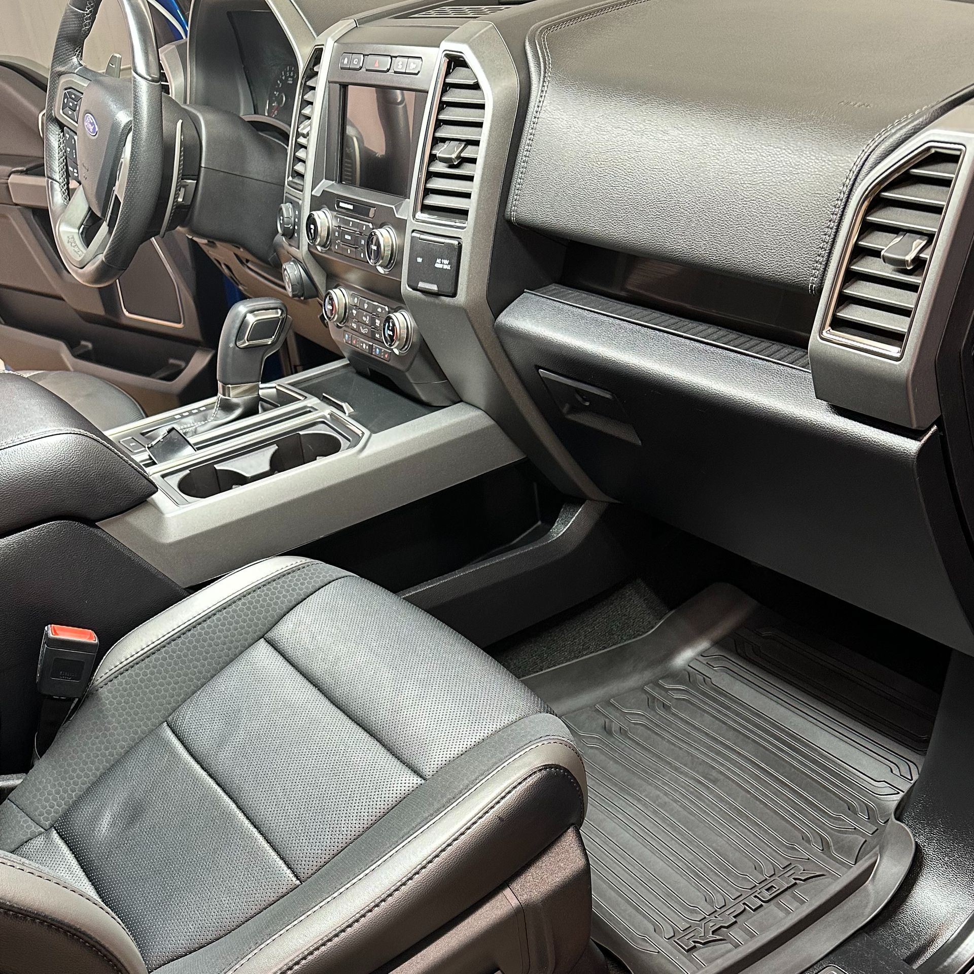 Interior of a black Ford truck showing dashboard, steering wheel, seats, and floor mats.