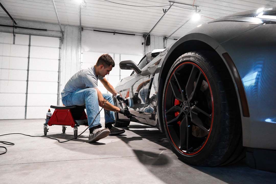 Man polishing a silver sports car's side in a garage. Red wheels, black tires.