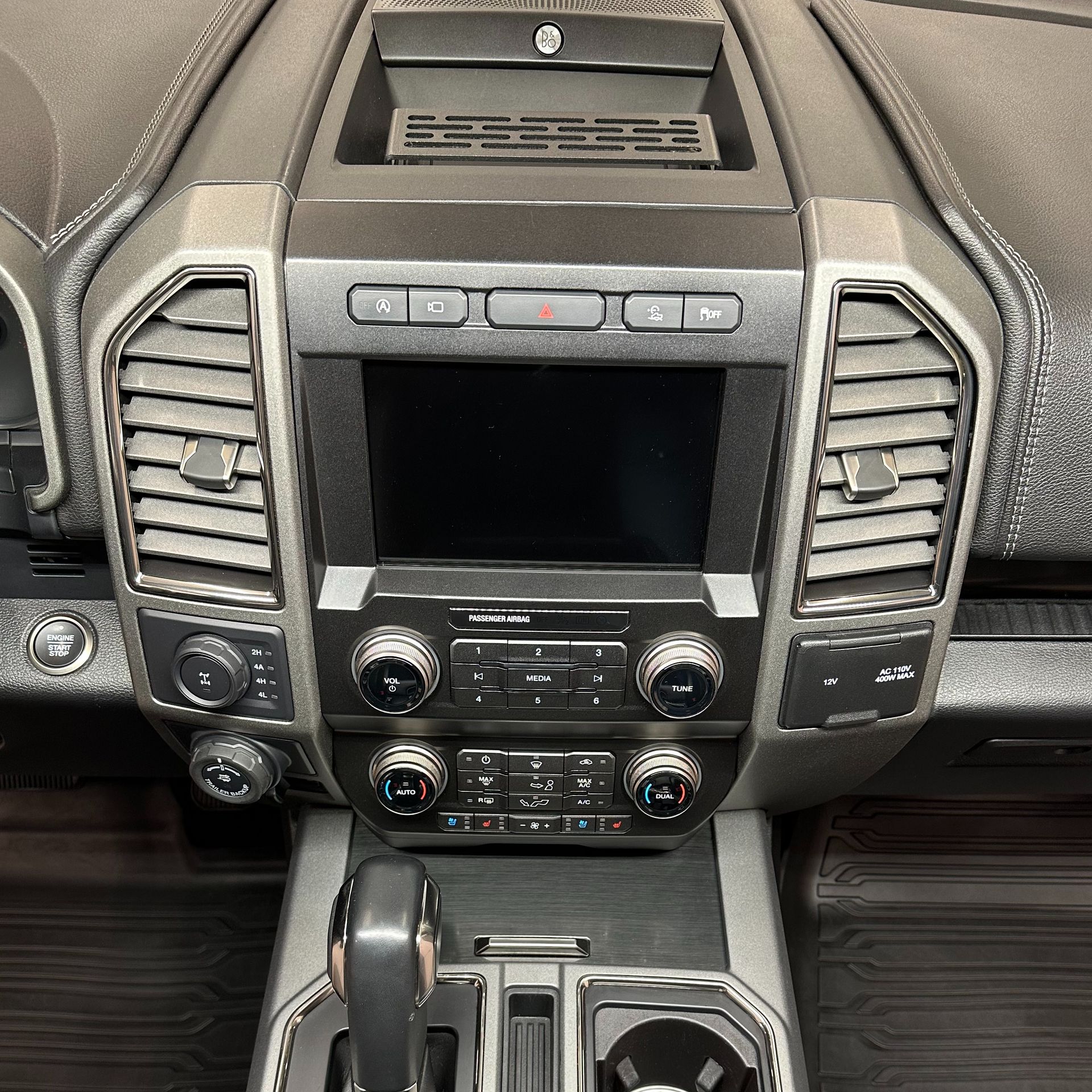 Car dashboard with screen, vents, controls, and gear shift. Black and gray interior.