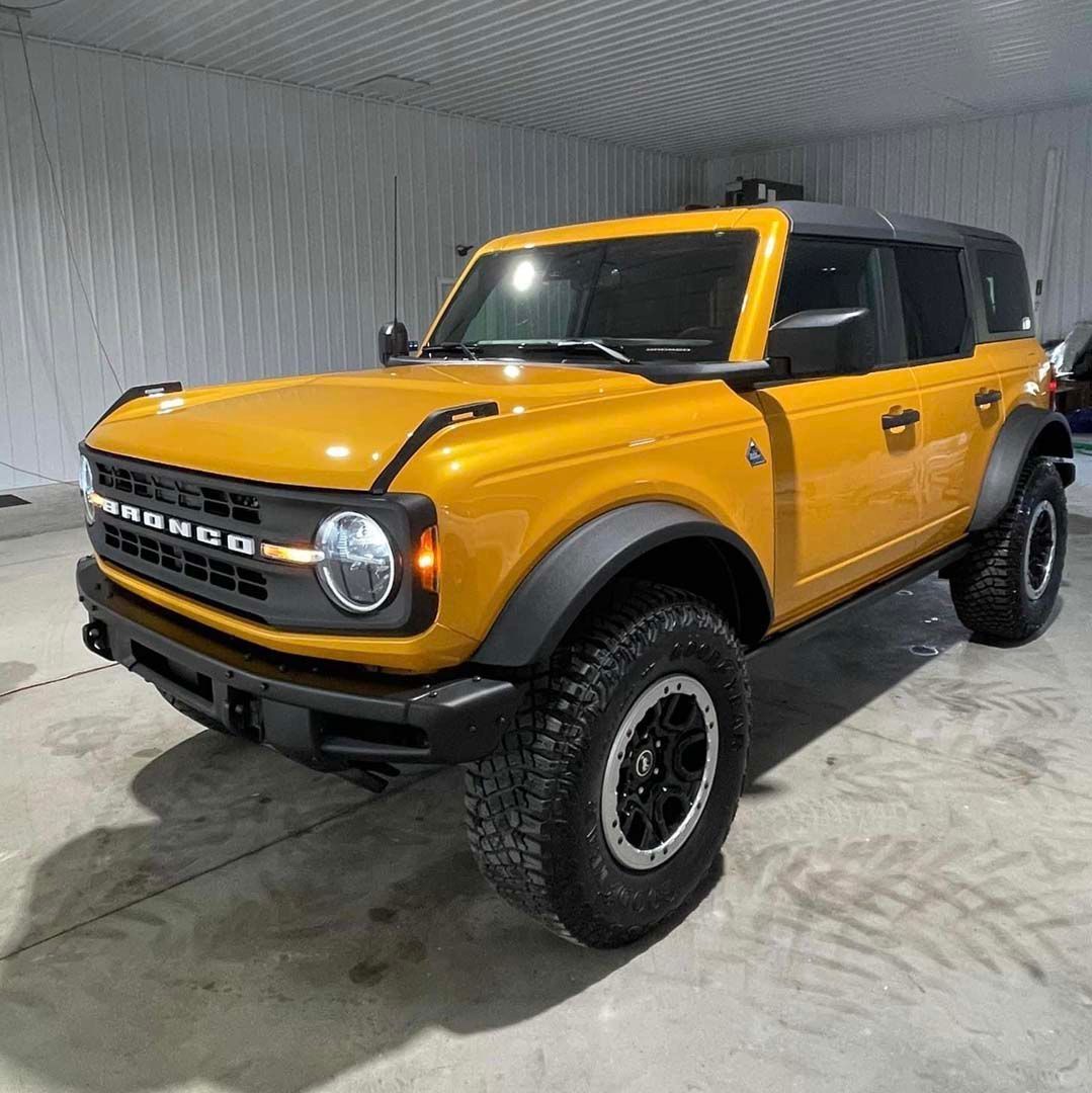 Yellow Ford Bronco SUV with black trim and large tires in a garage.
