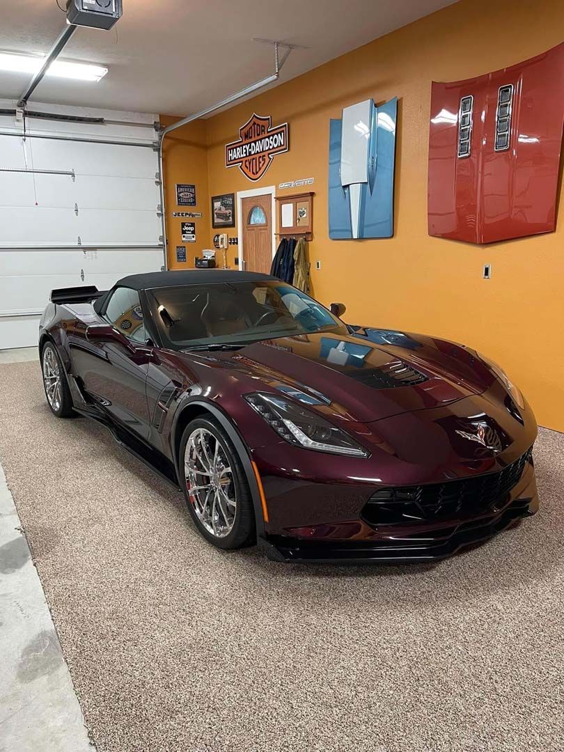 Burgundy Corvette convertible parked in a garage with epoxy flooring and orange walls.