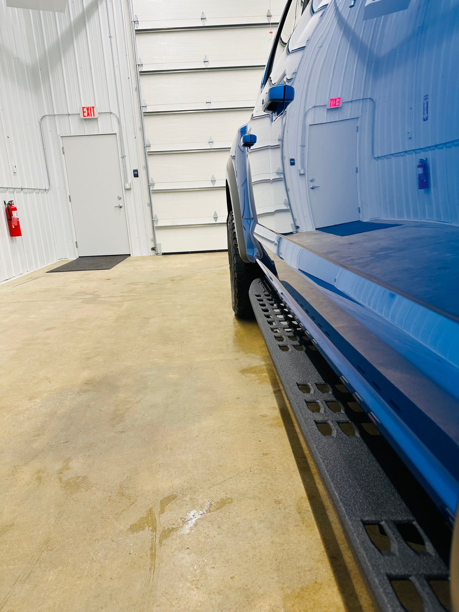 Blue pickup truck parked inside a garage, showing side step.