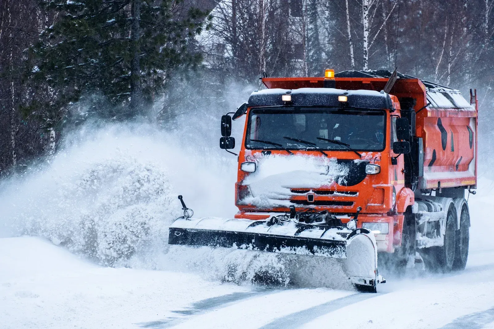A snow plow is driving down a snow covered road.
