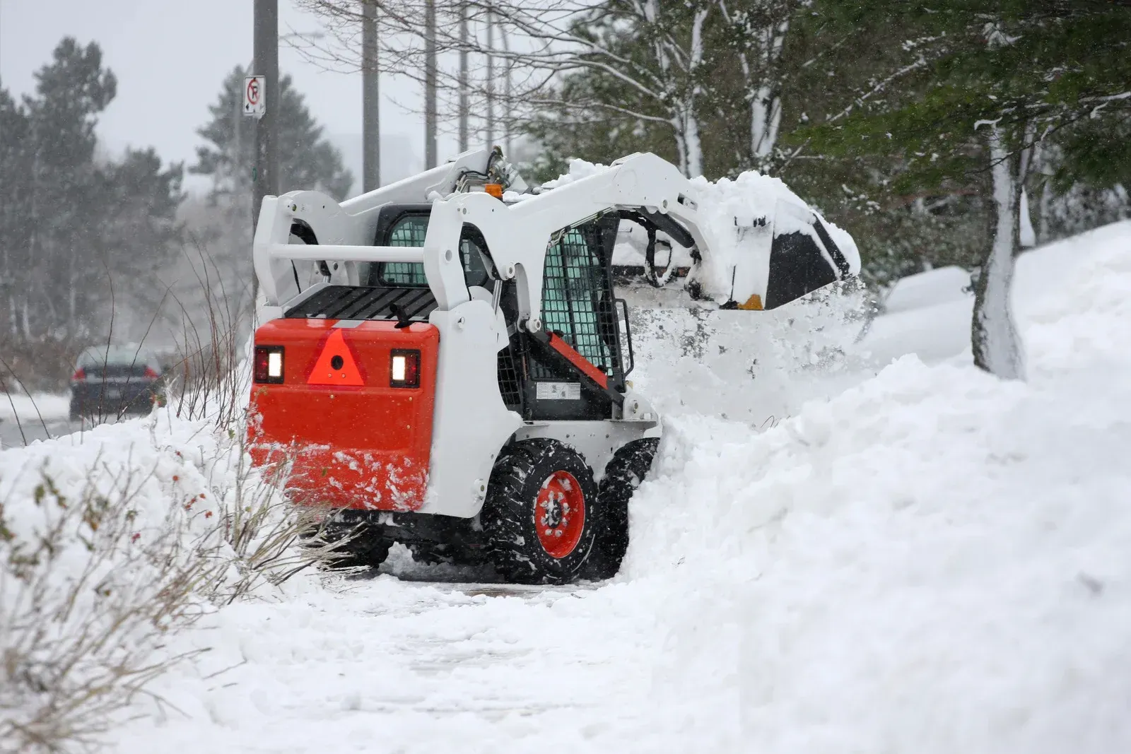 A snow plow is clearing snow from the side of a road.