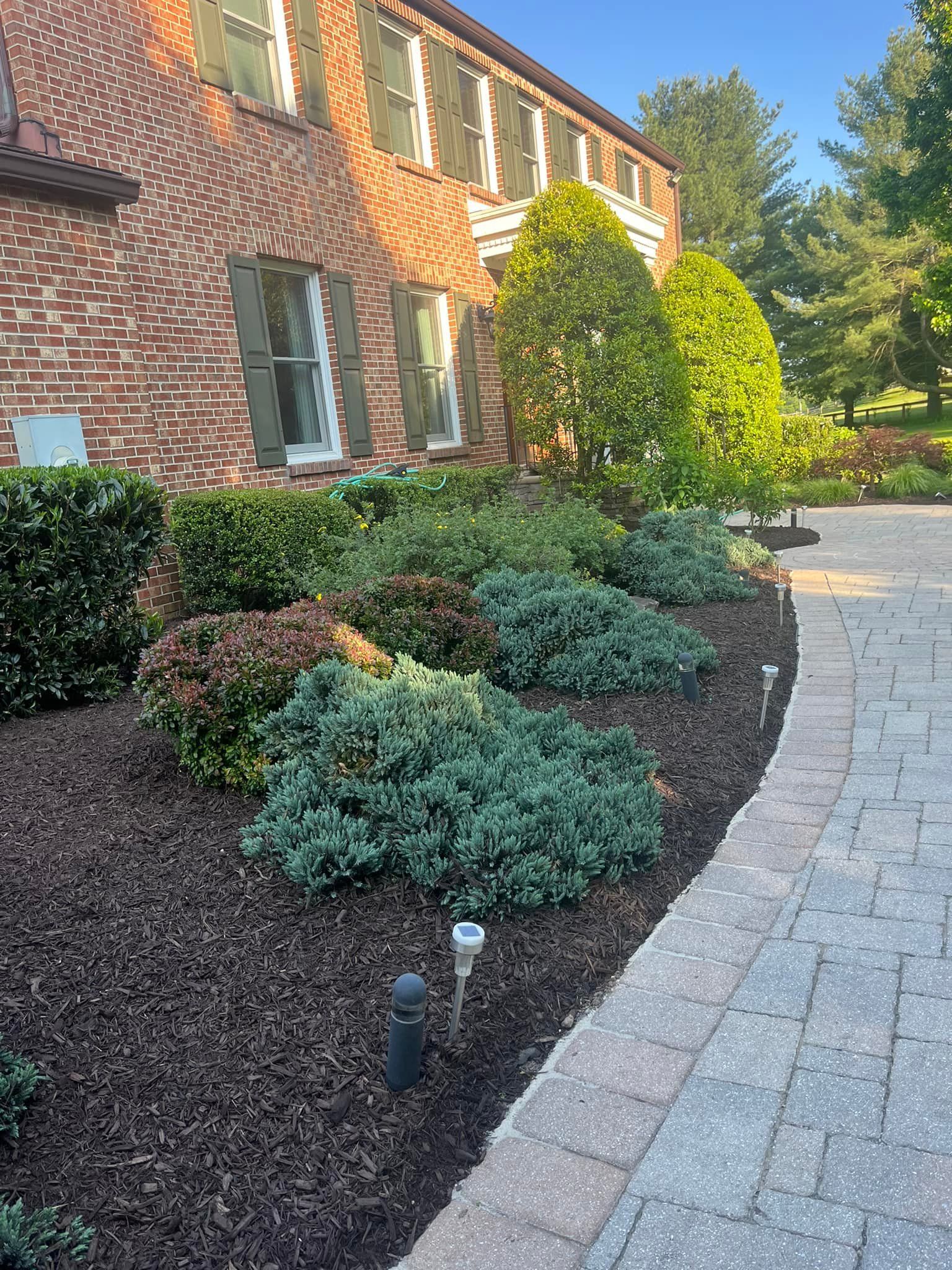 A brick house with a lush green garden in front of it.