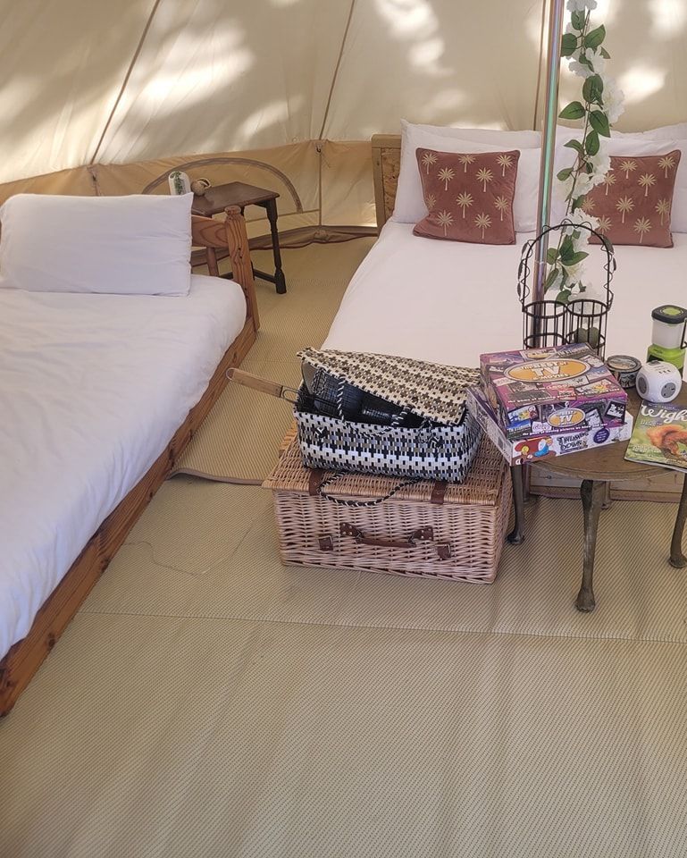 Cozy tent interior with two beds, pillows, and a small table with items like a basket and a jigsaw puzzle.