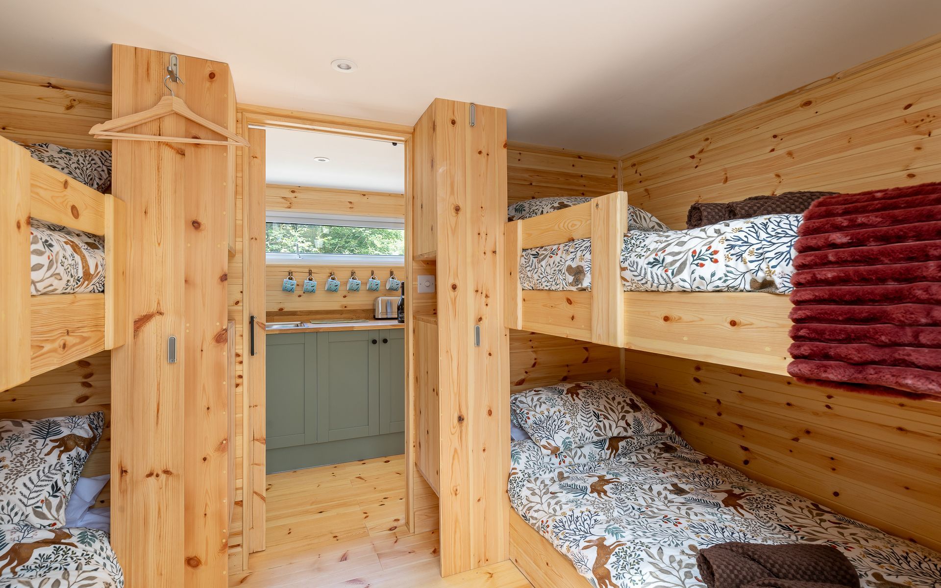 Interior of a cabin with multiple bunk beds made of light wood. There is a small kitchenette area visible.