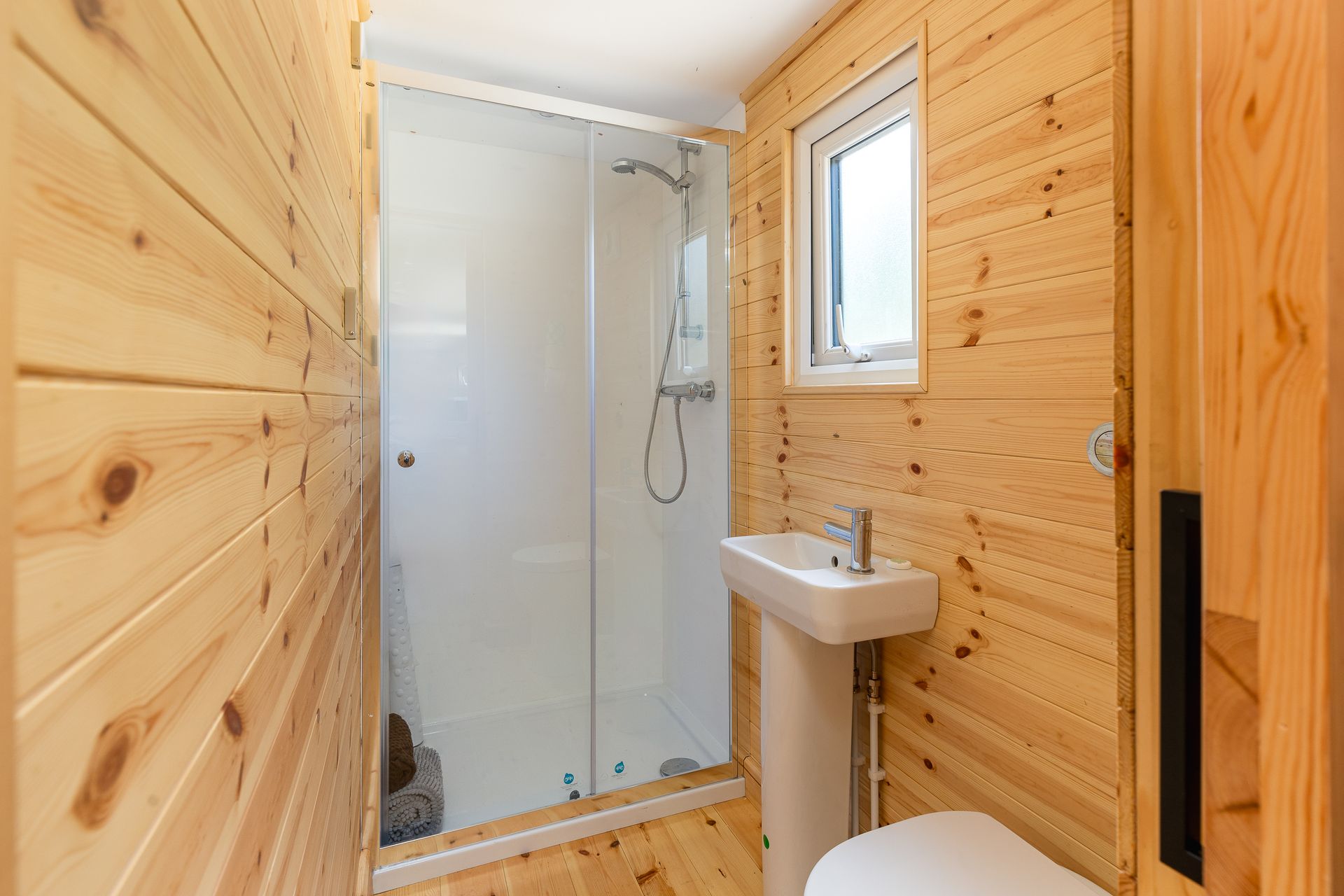 Small bathroom with wood paneling, shower, sink, and toilet.