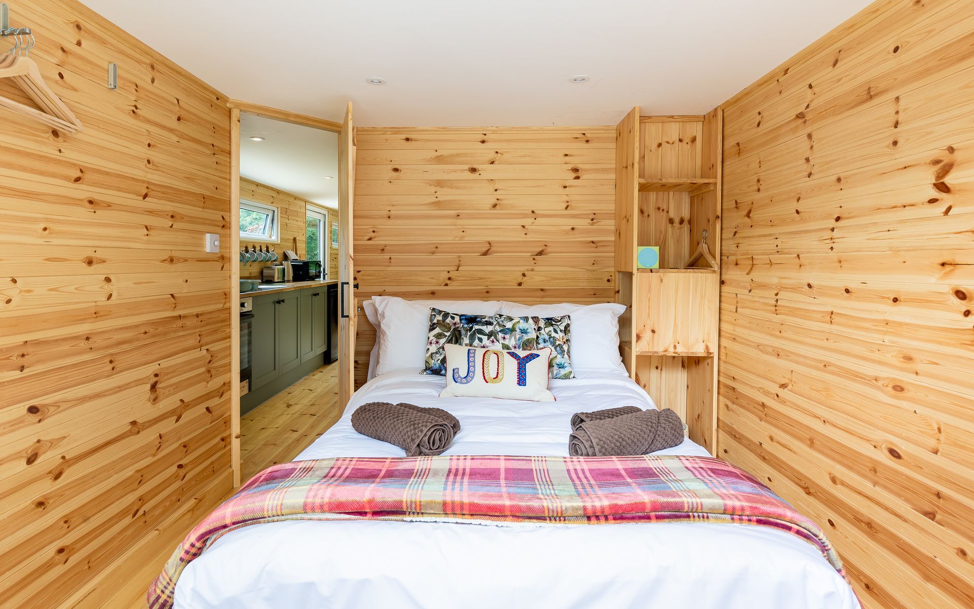 Cozy bedroom with wooden walls, double bed, and doorway to a kitchen.
