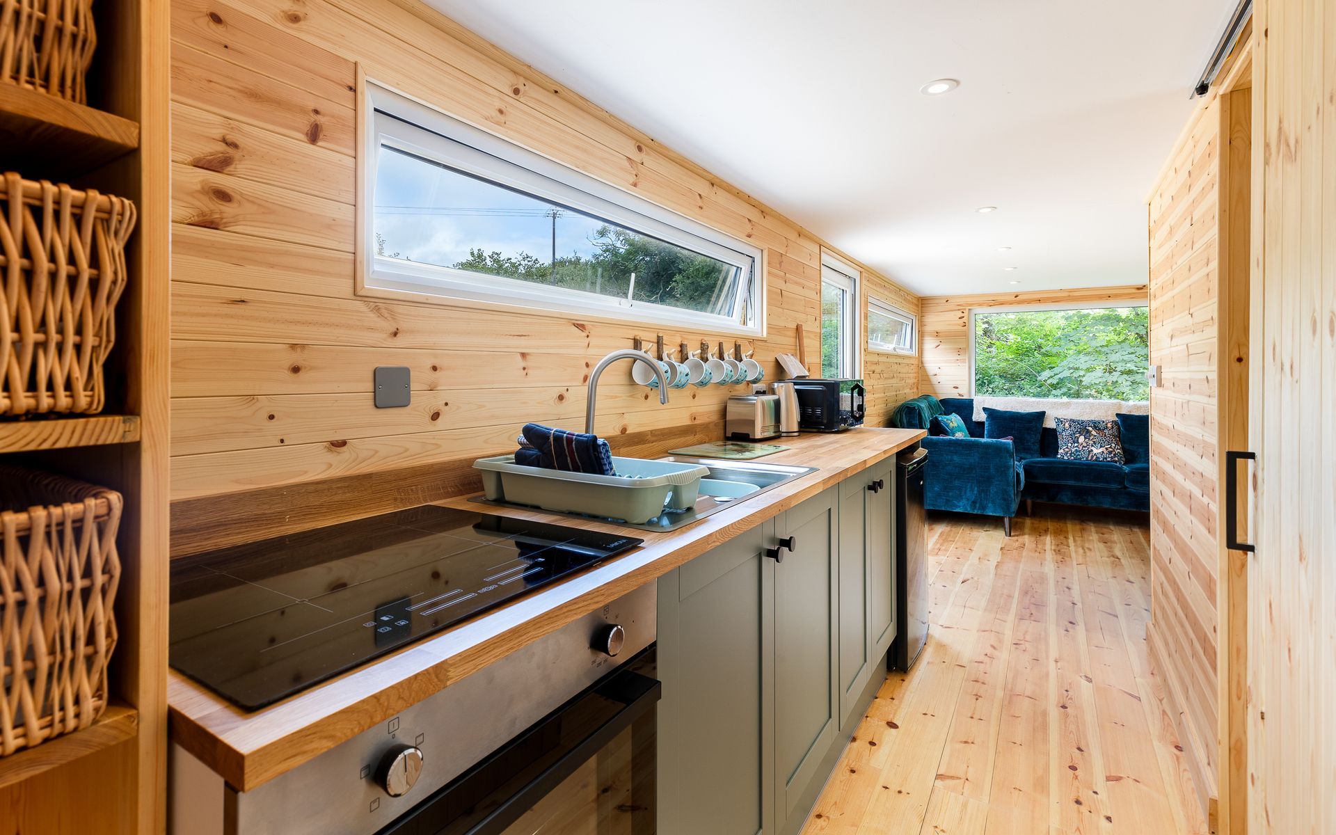 Kitchen interior with wooden walls, countertop, and appliances. A window and a living room in the background.