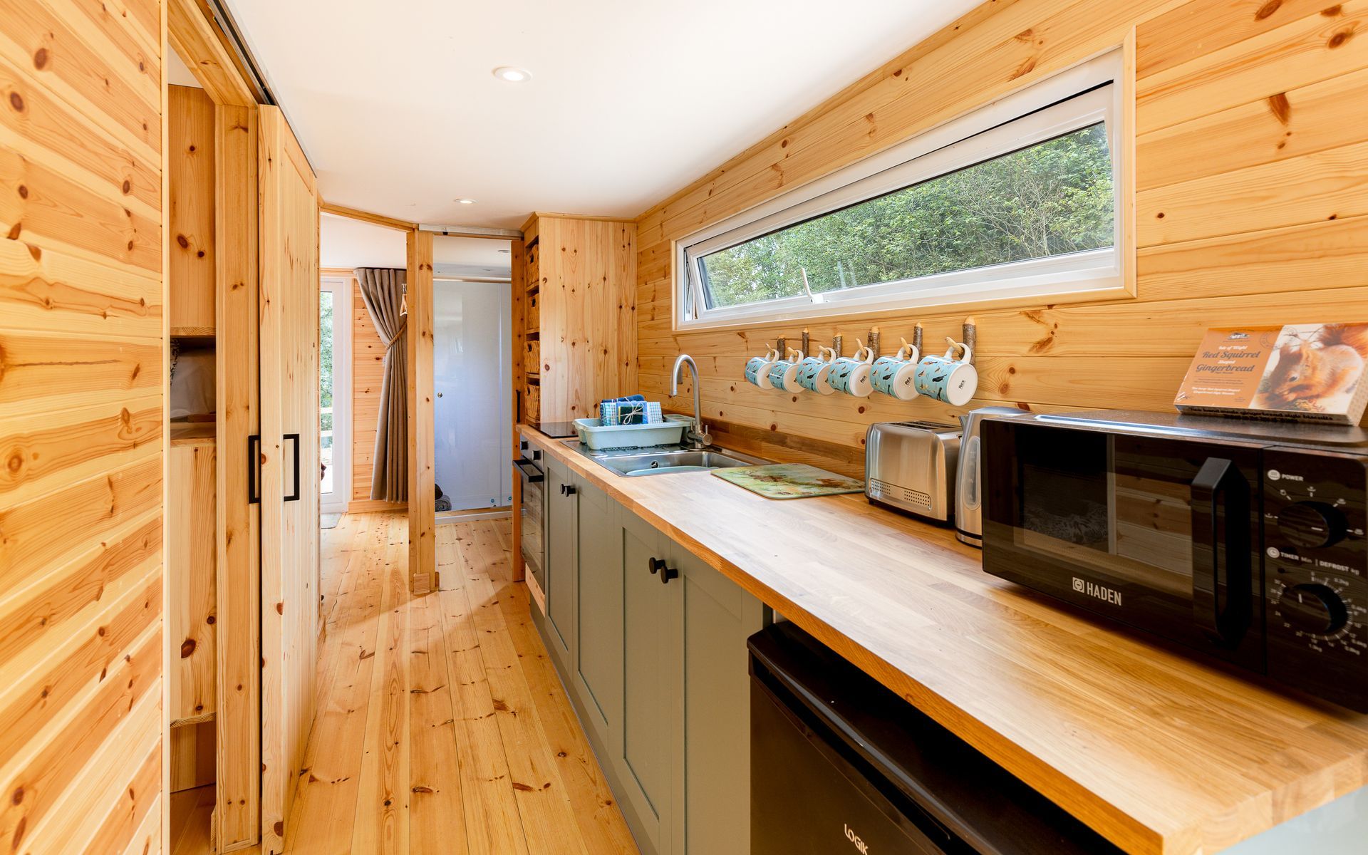 Wooden cabin interior with kitchen area and hallway. Natural light through the window.