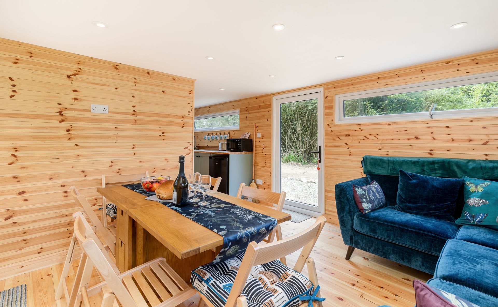 Interior cabin with wood paneling, dining table, blue sofa, and kitchen visible.