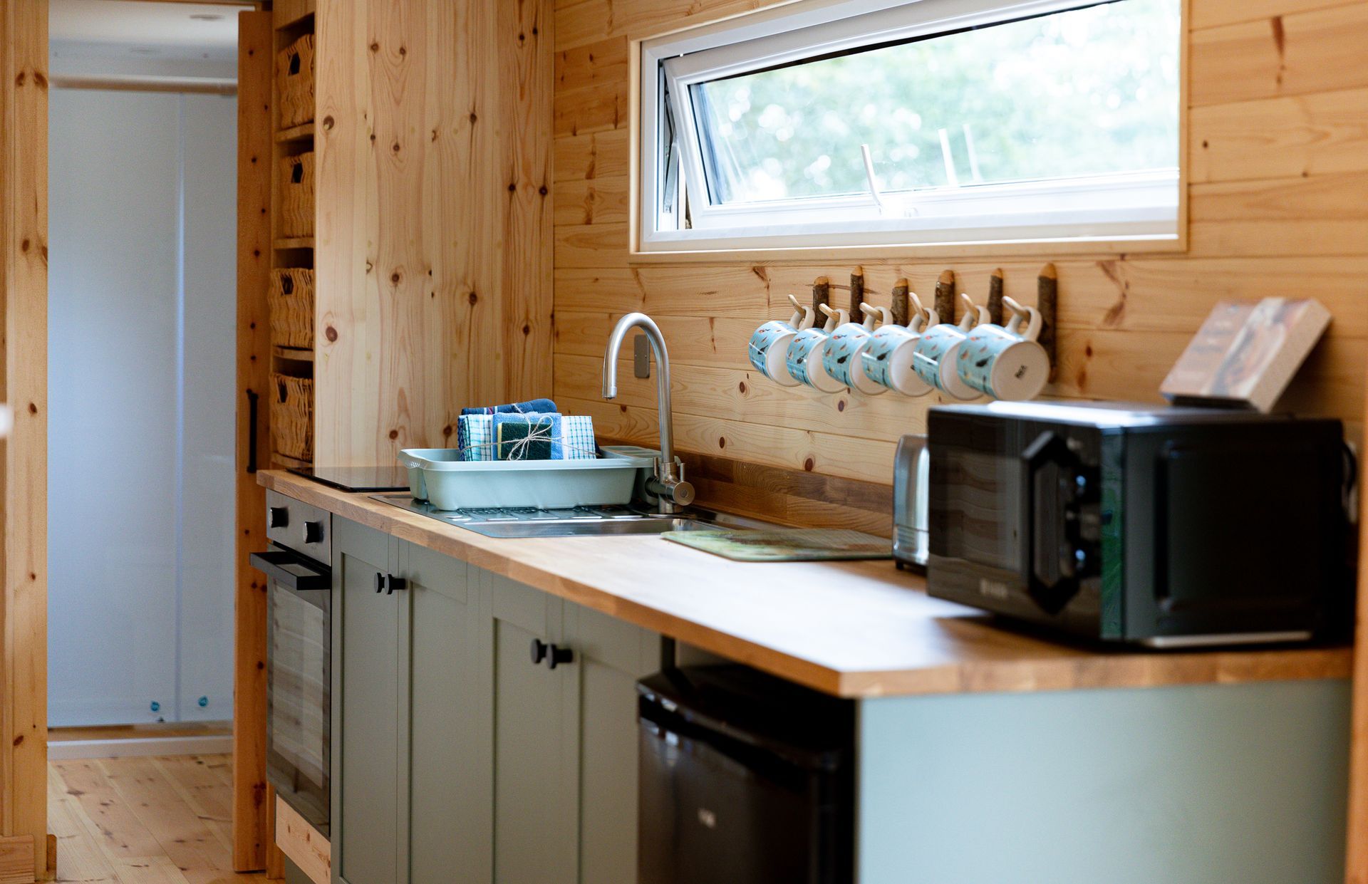 Cozy cabin kitchen with wooden walls, light-green cabinets, and a microwave and oven.