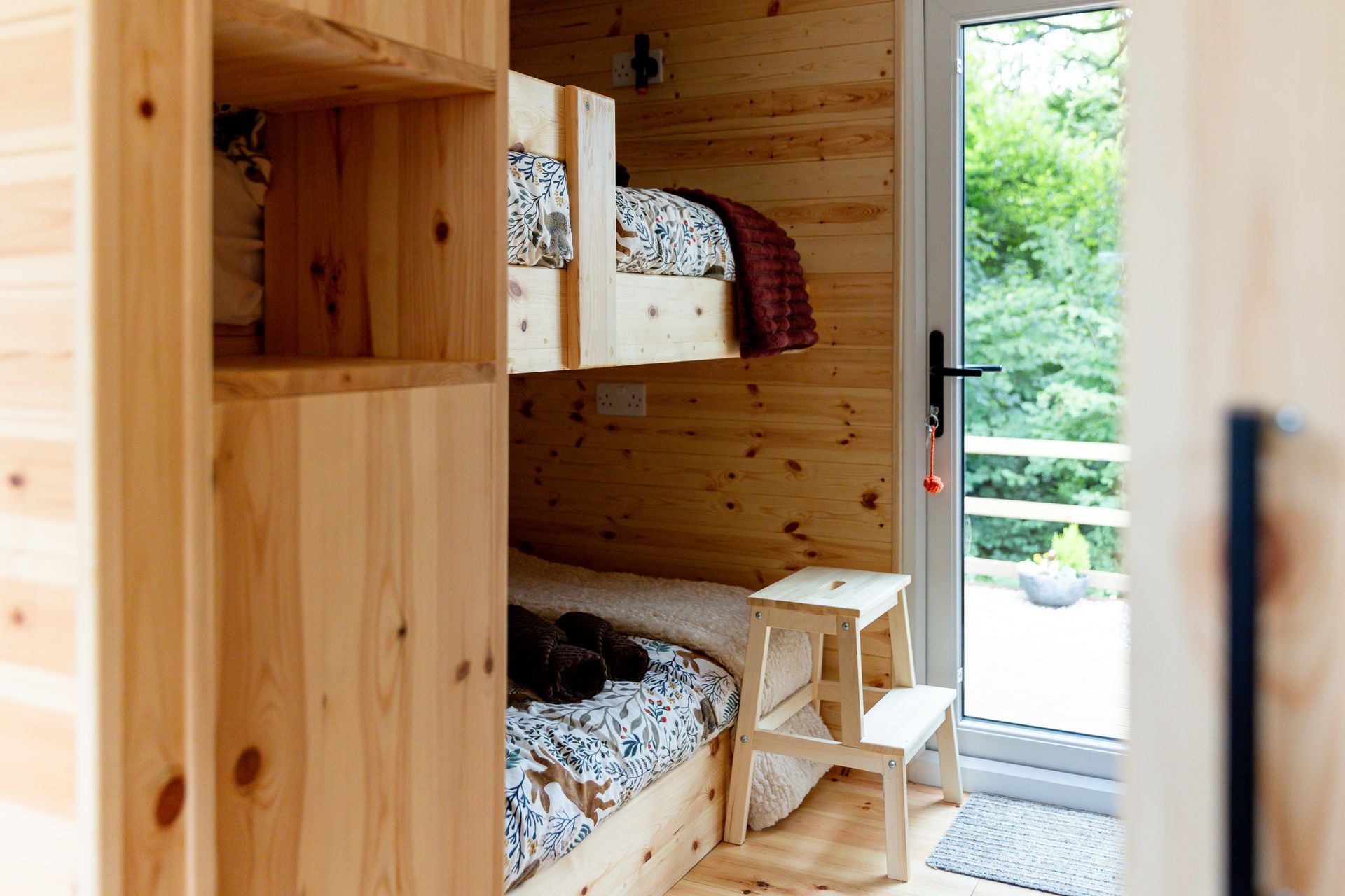 Wooden bunk beds in a cabin.  Doorway to exterior view.  Small wooden step stool. Natural wood tones.