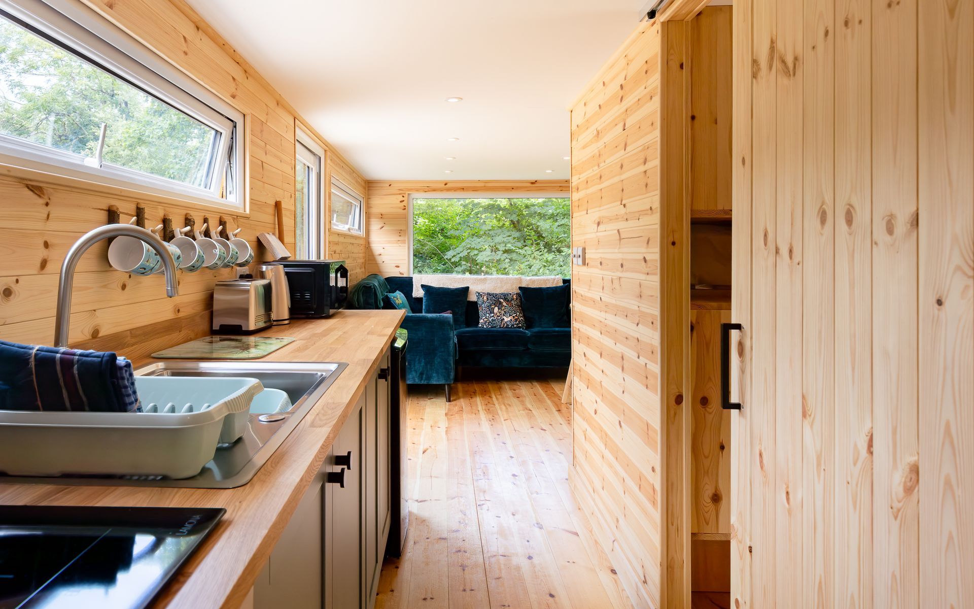 Interior of a wooden cabin with a kitchen, living area with a teal couch, and a sliding door.