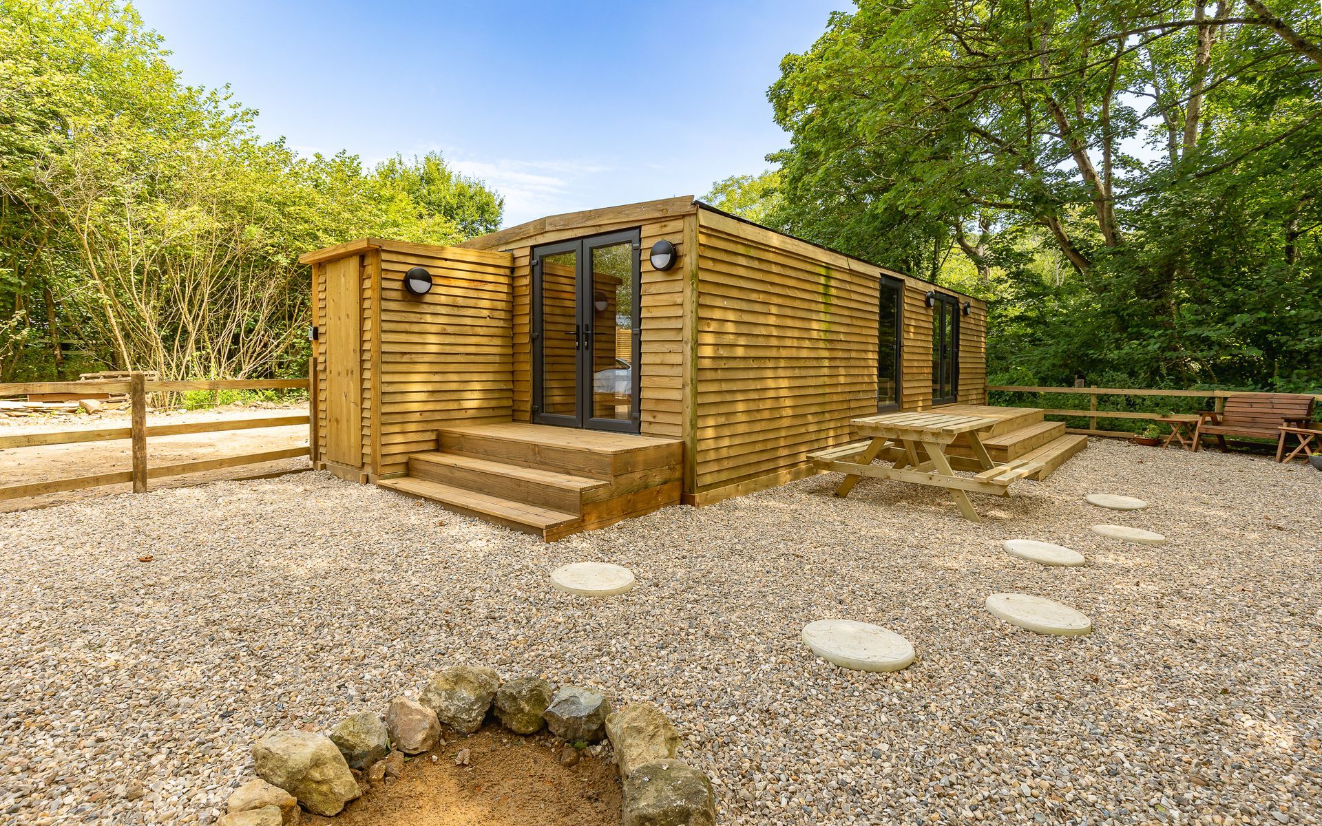 Wooden cabin with gravel ground, stone steps, and surrounding trees.