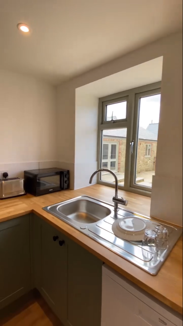 Kitchen with sink, window, wooden countertop, and appliances. Green cabinets and gray window frame.