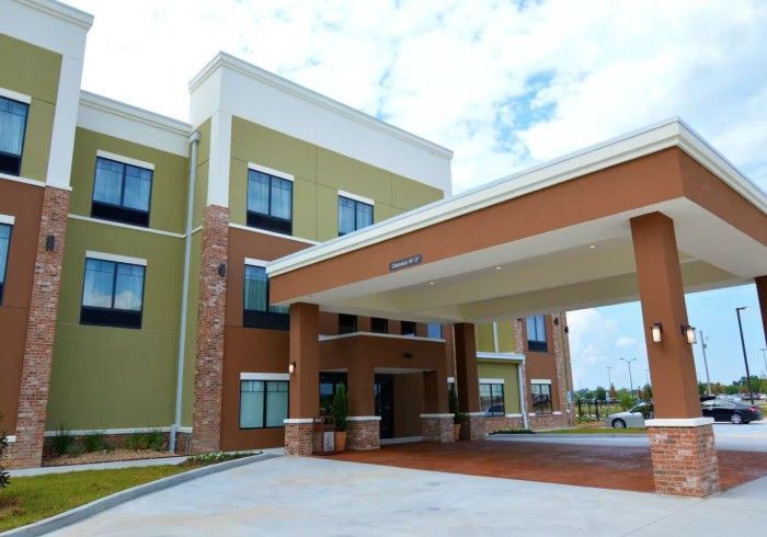 A multi-story hotel exterior with olive green and brown facade, stone pillars, and a large covered driveway entrance.