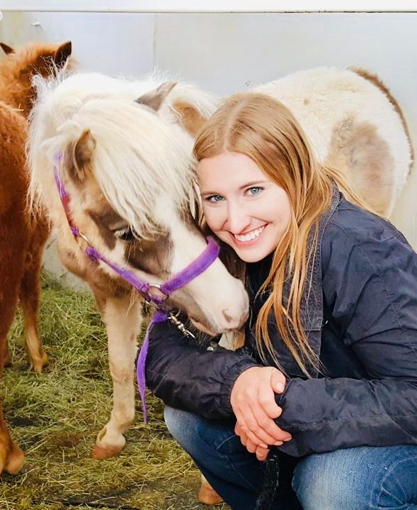 a woman is kneeling down next to a pony with a purple bridle .