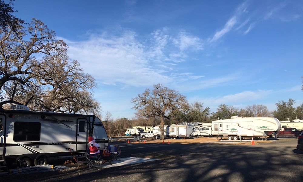 A lot of rvs are parked in a lot with trees in the background.