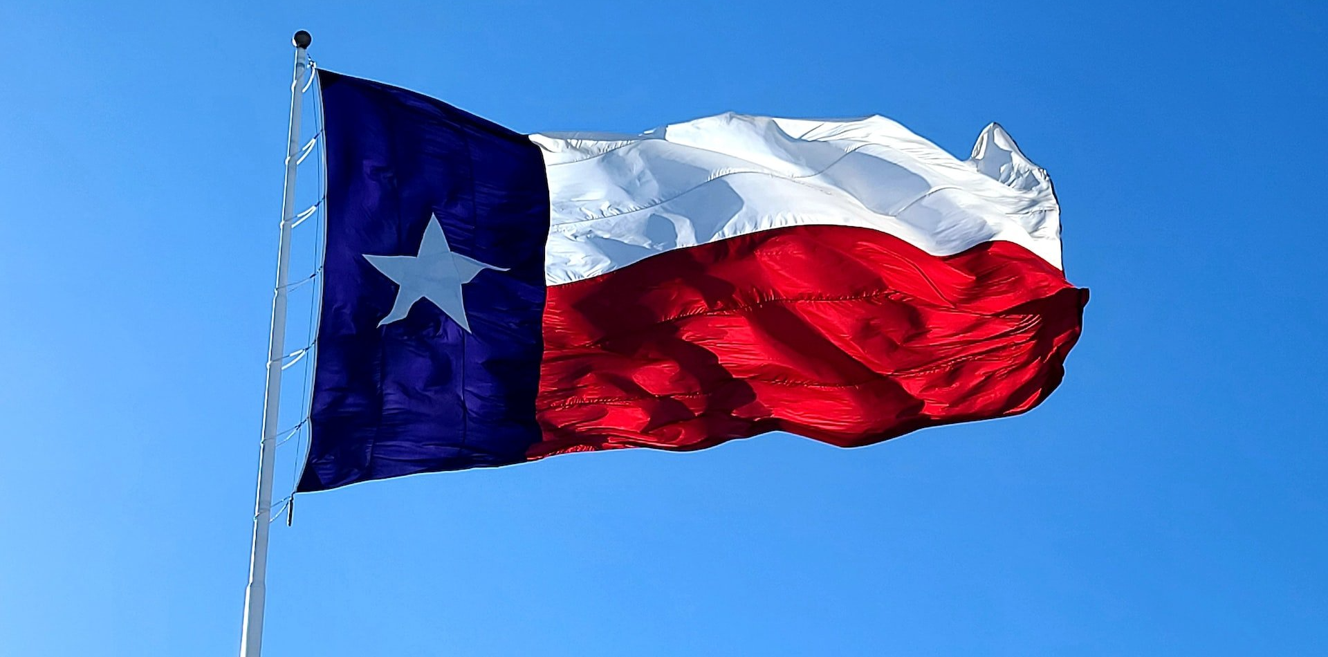 A texas flag is waving in the wind against a blue sky.