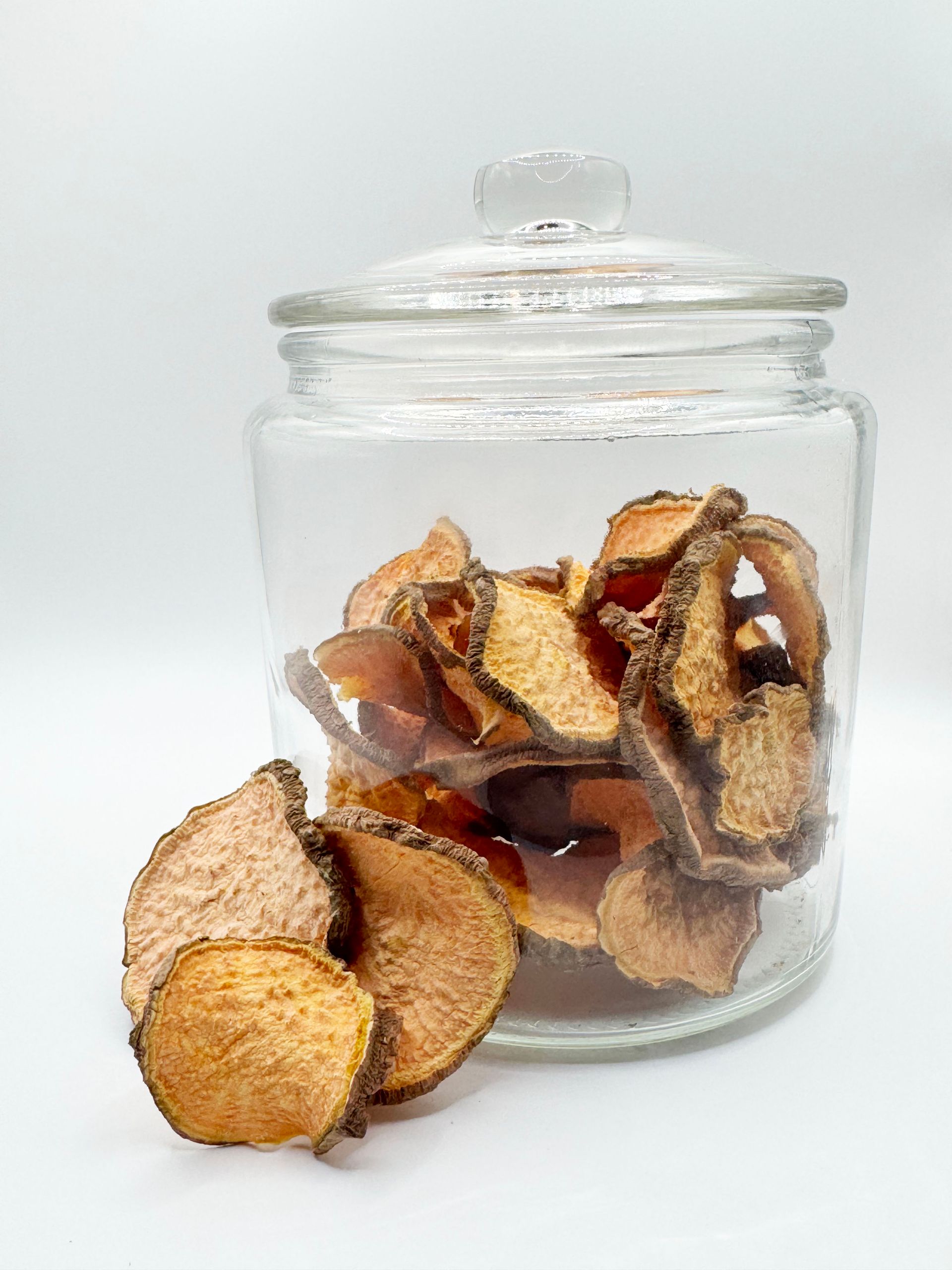 A glass jar filled with sweet potato chips on a white surface.