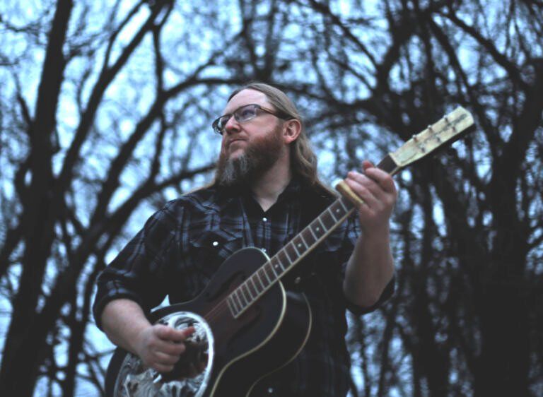 Image may contain guitar, man, glasses, trees