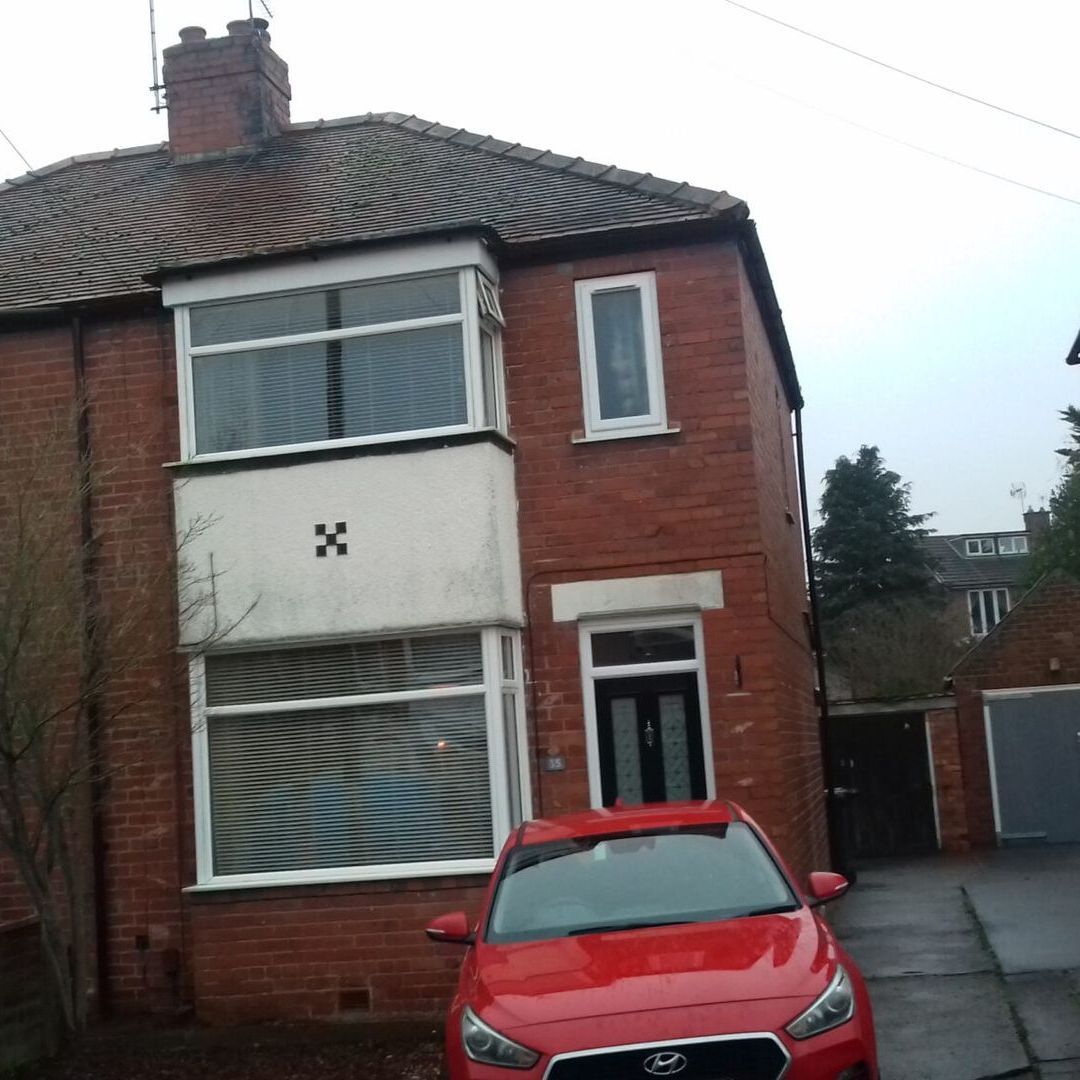 A red car is parked in front of a brick house