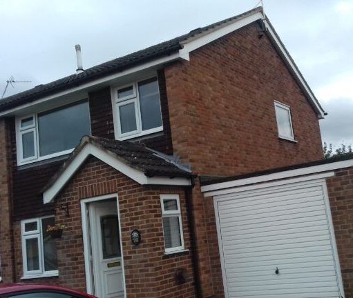 A red car is parked in front of a brick house with a garage.